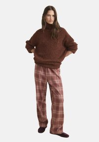 Braun strukturierter Strickpullover mit hohem Kragen, kombiniert mit rosa karierten weit geschnittenen Hosen, die ein gemustertes Design aufweisen.