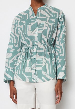 Koszula na guziki z długim rękawem w turkusowo-biały abstrakcyjny geometryczny wzór, wiązana w talii, zestawiona z białymi szortami.