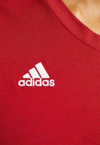 Gros plan sur un tissu rouge avec le logo Adidas brodé en blanc et une partie d'un col.