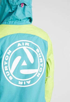 Person trägt eine türkis- und hellgrüne Jacke mit Kapuze, mit einem großen weißen runden "Burton Air" Logo auf dem Rücken.