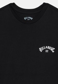 Must must tshirt, mille ümmarguse kaelusega, millel on vasakul rinnal valge "Billabong" logo kaarekujunduses.