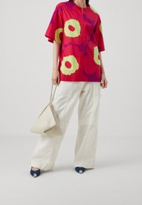 Lys rød kortærmet skjorte med store gule og lilla blomster mønstre, parret med loose hvide cargo bukser og marineblå hæle. Bærer en cremet håndtaske.