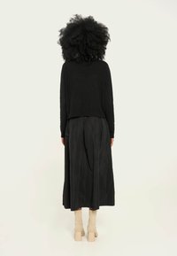 Pullover negru scurt, fustă neagră fluidă, botine crem până la glezne. Puloverul are tiv cu dungi, fusta are pliseuri. Texturi fine, design minimalist.