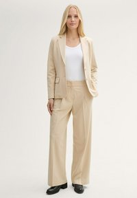 Blazer ajustado beige y pantalones de pierna ancha combinados con una camiseta sin mangas blanca. Tela suave con un detalle mínimo y acentos en calzado negro.