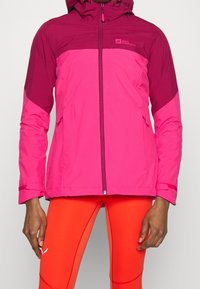 Roze waterdichte jas met capuchon, met een donkerder roze bovenstuk, rits aan de voorkant en zijzakken. Glad oppervlak, sportieve pasvorm.