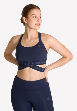 Marineblauwe sportbeha met een kruisbandontwerp, een brede gemerkte band en een gladde textuur. Gecombineerd met bijpassende hooggetailleerde leggings.