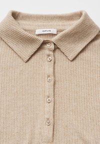 Beige geribd gebreid poloshirt met een omslagkraag en vijf bijpassende knopen op de voorste knoopsluiting, het label draagt de tekst "OPUS".