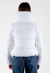 Giacca bianca imbottita con colletto alto, design trapuntato e finitura elegante. Indossata su jeans di denim, mostrando una vestibilità rilassata e una consistenza.