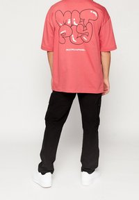Camiseta de coral de gran tamaño con un atrevido texto gráfico en negro en la parte posterior, combinada con pantalones cargo negros y zapatillas blancas. Textura de algodón suave.