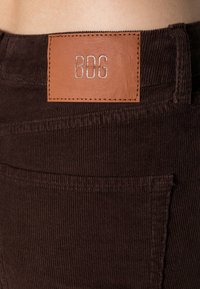 Calças de pêlo de corduroy castanho com uma superfície texturizada, apresentando um rótulo em pele da BDG na cintura e um bolso traseiro.