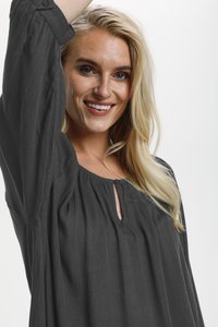 Blouse noire texturée avec un col rond, des boutons décoratifs et un tissu froncé. Manches longues avec des boutons aux poignets.