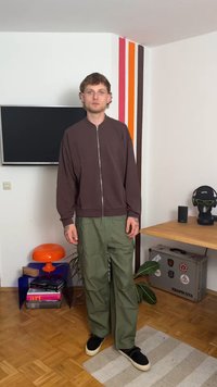 Brown zip-up bomber jacket, green cargo pants, black shoes. Smooth fabric, relaxed fit, noticeable details include zipper and pockets.