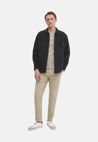 Camisa negra de botones sobre un suéter beige de cuello redondo, combinada con pantalones caqui claros y zapatillas blancas. Tejido suave con dos bolsillos en el pecho.