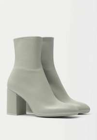 Zielone botki do kostek wykonane z gładkiego materiału syntetycznego, z wąskim noskiem i prostokątnym obcasem blokowym dla dodatkowego wsparcia.