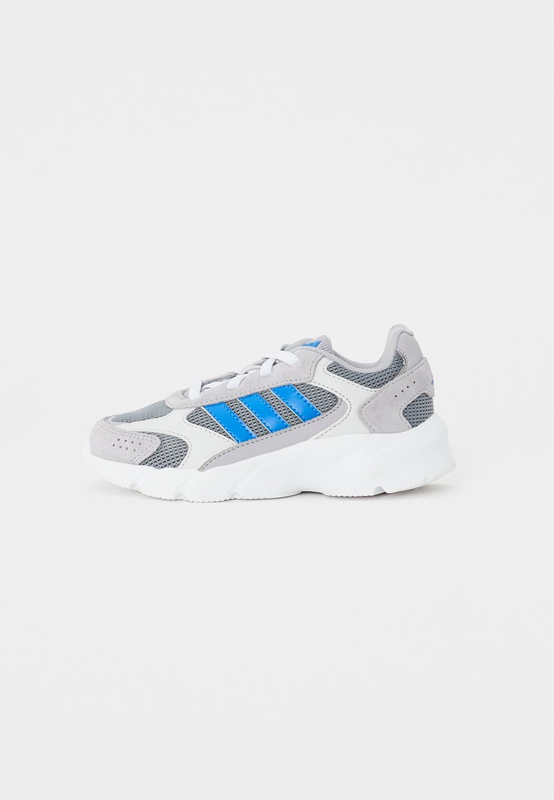 Zapatilla deportiva gris que combina materiales de malla y ante, con rayas de acento azules, suela de goma blanca y diseño de cordones.