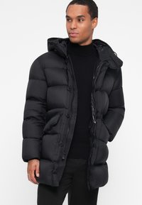 Giacca a vento nera con cappuccio, chiusura con zip e bottoni, e texture trapuntata. Progettata con tasche laterali e una silhouette elegante.
