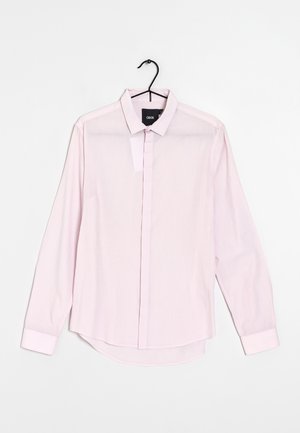 Camicia rosa chiaro a maniche lunghe con colletto, orlo dritto e una texture di tessuto liscia, leggermente trasparente.
