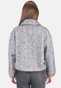 Graue, grob gestrickte Jacke mit strukturiertem Finish, weitem Kragen und lockerer Passform. Der Rücken verfügt über überschnittene Schultern und seitliche Taschen.