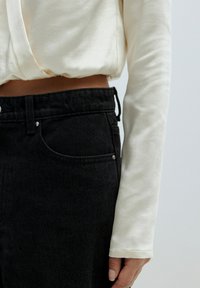 Lichtcrème lange mouwen top met een gladde textuur, gecombineerd met hoge zwarte denim jeans met een trekkoord en minimale accenten.
