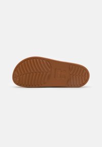 Semelle de chaussure en caoutchouc brun avec des motifs texturés pour une meilleure adhérence, dotée d'un logo central et d'accents en relief pour la traction et la durabilité.