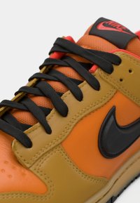Nike sneakers featuring a blend of orange and tan leather with black accents, textured mesh, and black laces, detailed stitching, and logo.