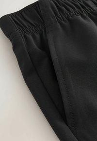 Svarta sportbyxor med elastisk midja, sl�ät yta och subtila sömnadsdetaljer, som visar en figurnära design och funktionell stil.