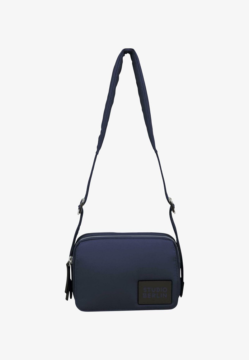 Marineblå crossover taske lavet af holdbart materiale, med en slank rektangulær form, lynlås lukning og et logo patch samt en justerbar rem.