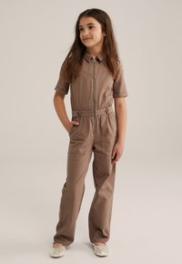 Jumpsuit de algodón marrón con mangas cortas, cierre de cremallera en el frente y detalles de botones en la cintura. Cuenta con dos bolsillos laterales y un diseño de pierna recta.