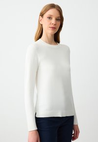 Maglione bianco a maniche lunghe realizzato in un morbido tessuto a maglia. Presenta un collo rotondo e polsini a coste. Design semplice e classico senza pattern visibili.