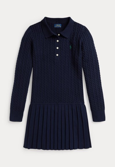 Σαλοπέτα ναυτικού στυλ με πλέξη και μακριά μανίκια, πόλο γιακά, τέσσερις κουμπιά μπροστά και πλισέ φούστα. Διαθέτει πράσι�νο λογότυπο στο στήθος.