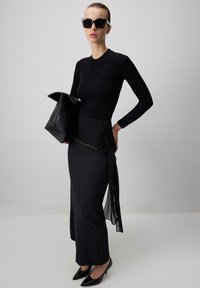 Top a maniche lunghe fitted nero abbinato a una gonna nera con sovrapposizione trasparente e borchie dorate. Accessoriato con una borsa in pelle nera e tacchi.