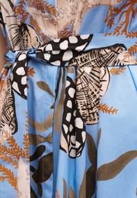 Μπλε ύφασμα με μαύρα, λευκά, μπεζ και καφέ αφηρημένα σχέδια φύλλων και φτέρων δεμένα κόμπο στη μέση.