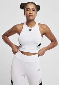 Crop top de sport blanc avec accents noirs et logo ; assorti à un legging blanc taille haute avec des détails noirs et gris.