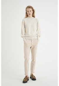 Beige pletený svetr s kulatým výstřihem, volnými rukávy, v kombinaci s přiléhavými světle růžovými kalhotami a hnědými koženými polobotkami. Jednoduchý design, hladká textura.