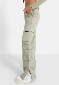 Pantalons cargo vert clair avec plusieurs poches, design de jambe fuselée et fentes latérales ; associés à des baskets blanches épaisses avec des accents pastel.