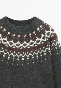Pull en laine gris foncé à col rond, présentant des motifs géométriques à tricots jacquard blancs et bordeaux sur le yoke et les épaules.