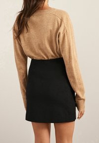 Tans brei sweater en zwarte minirok. De sweater heeft geribbelde boorden en een ronde halslijn. De rok is nauwsluitend met een gladde textuur.