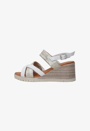Wedge sandals with a white leather upper and metallic gold accents. Features crisscross straps and a textured wedge heel with a beige sole.