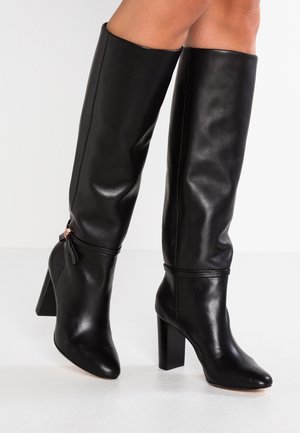 Black leather knee-high boots with a pointed toe, chunky block heel, ruching detail at the top, and a small decorative strap with hardware.