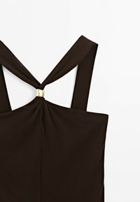 Black sleeveless top with wide straps crossing and gathered at the center with a small gold square embellishment.