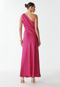 Fuksijos spalvos su viena petneša ilga suknelė, pagaminta iš sklandžios, lanksčios medžiagos. Suknelė turi prigludusią liemenį ir platėjantį sijoną, derinasi su pasmauktais aukštakulniais.