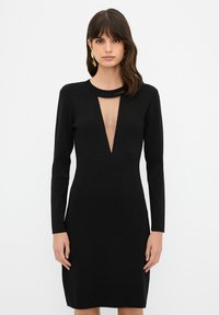 Schwarzes Kleid aus Strickstoff mit langen Ärmeln und einem tiefen V-Ausschnitt mit Ausschnittdetail. Figurbetonte Silhouette, glatte Textur.