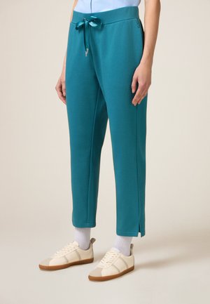 Pantaloni jogger verde acqua realizzati in tessuto morbido con vita regolabile e spacchi laterali, abbinati a sneakers crema e calzini bianchi alla caviglia.
