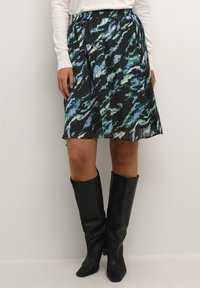 Jupe plissée noire avec un motif abstrait bleu et vert, dotée d'une taille élastique. Assortie à des bottes noires montantes.