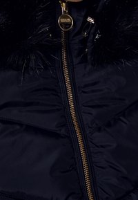 Námořnická péřová bunda s odnímatelným černým umělým kožešinovým límcem, zlatým zipem a diagonálním prošíváním panelů pro texturovaný detail.