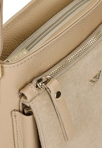 Borsa beige con una combinazione di pelle testurizzata e morbida suede. Presenta una chiusura con zip superiore, hardware in tonalità oro e una tasca laterale.