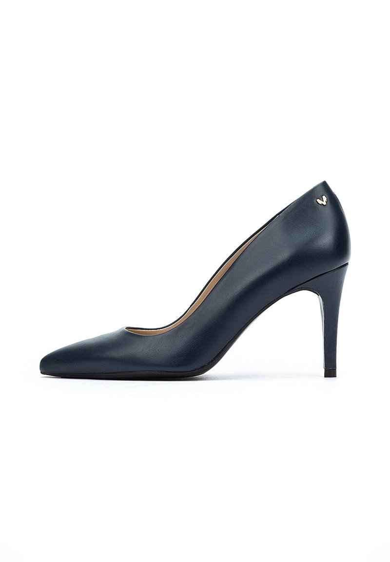 Zapato de tacón alto de cuero azul marino con puntera puntiaguda, tacón de aguja delgado y sutil acento de logo dorado en la parte posterior.
