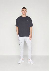 Juodas medvilninis marškinėlis laisvo kirpimo, derinamas su baltais sportinėmis kelnėmis, kurios turi juodų detalių, ir baltais sportiniais bateliais.