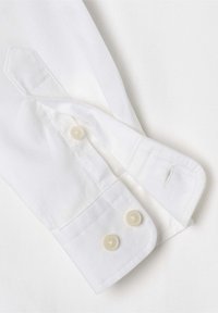 Polsino di camicia bianco con due bottoni rotondi di colore chiaro, forma a polsino appuntito e cuciture visibili lungo i bordi. Texture liscia.