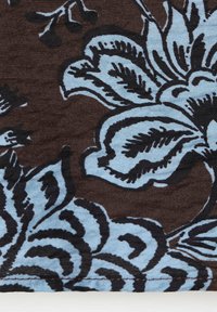 Gros plan d'un tissu avec des motifs floraux bleus et noirs sur un fond brun foncé, montrant des coutures détaillées le long du bord.